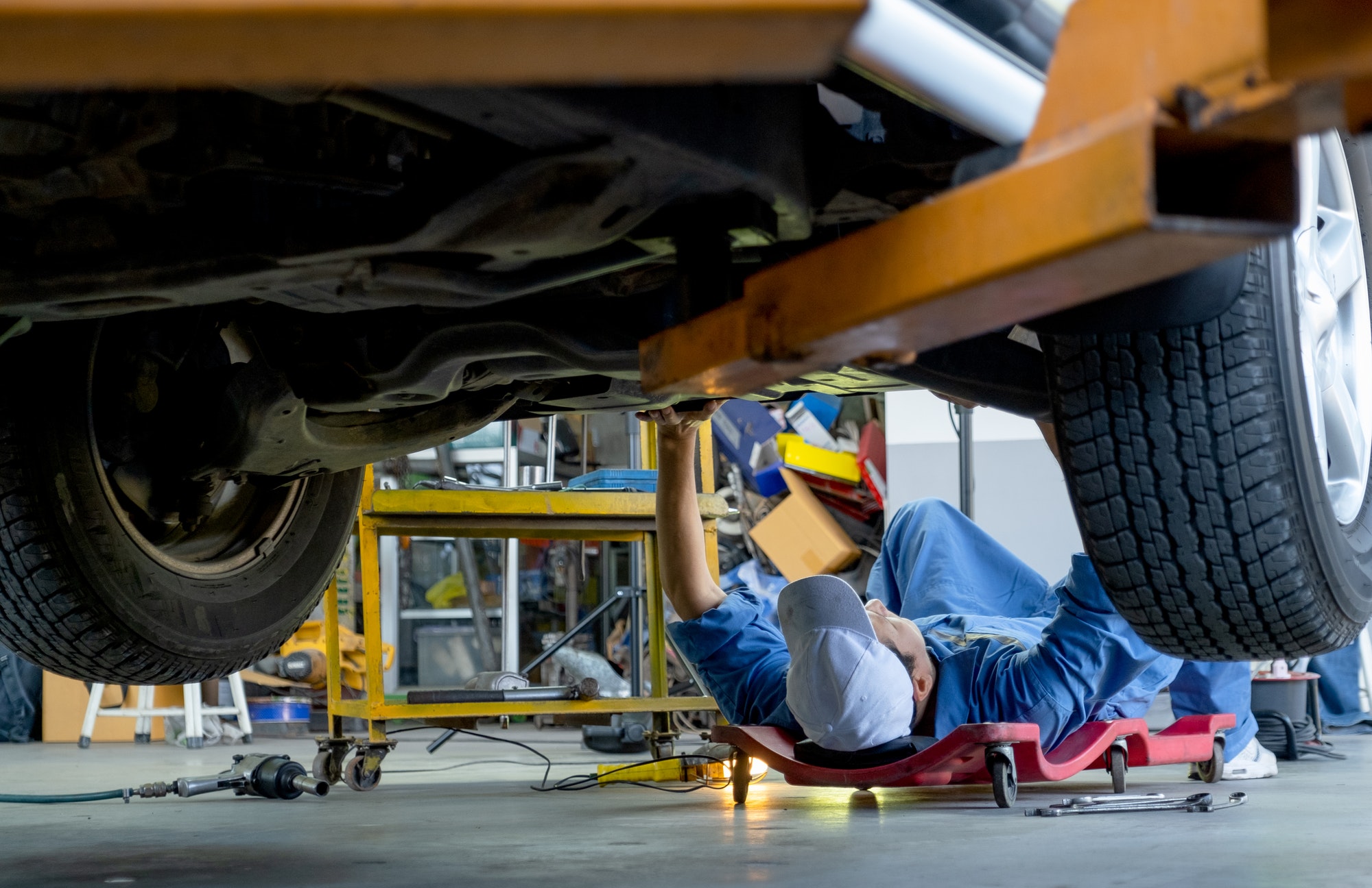 Vue inférieure sous le garage automobile ou le technicien s'allonger et vérifier le problème dans la zone de travail.