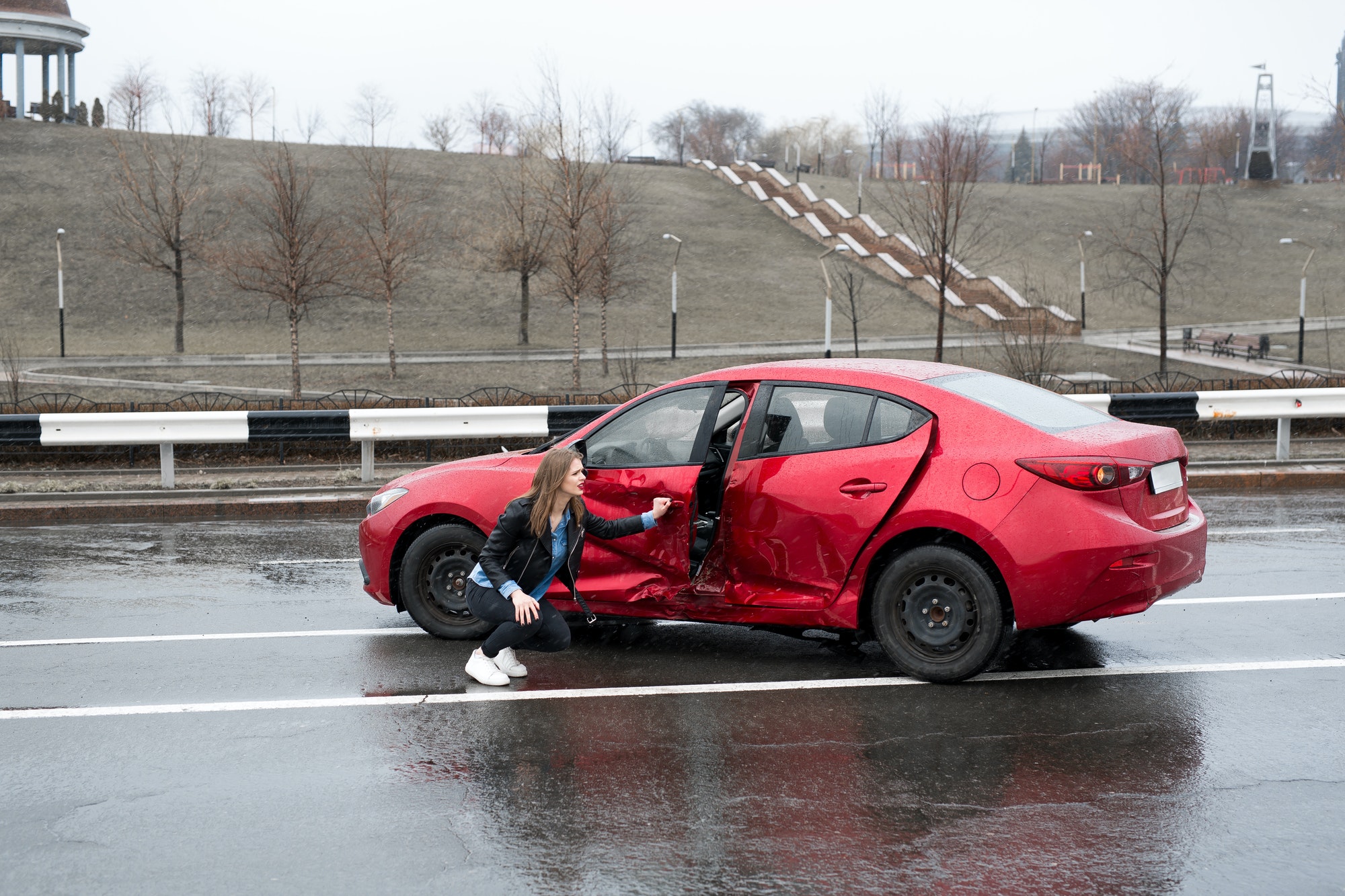 Une femme est assise près d'une voiture cassée après un accident. 